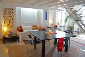 Een ruime woonkamer met een bank, een eettafel en een trap.