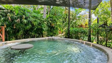 Relax in a serene hot tub surrounded by lush tropical vegetation and a natural canopy.