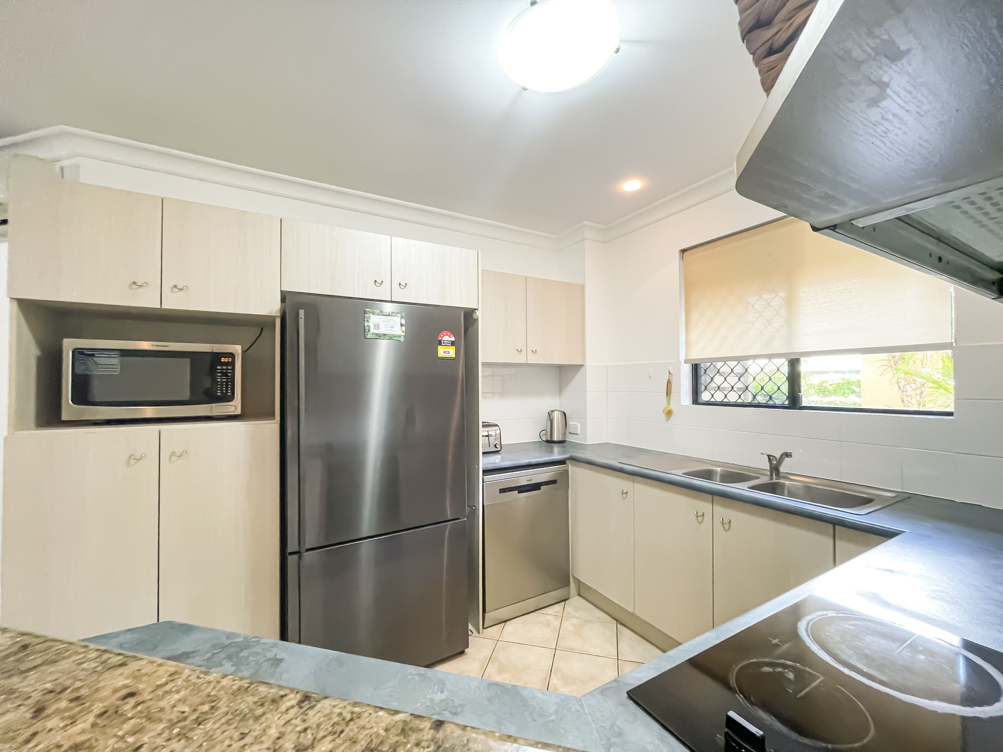 A modern kitchen with white cabinets, a stainless steel refrigerator, a microwave, a toaster, and a sink.