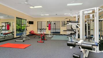 A gym with ceiling fans, exercise equipment, and a red mat.
