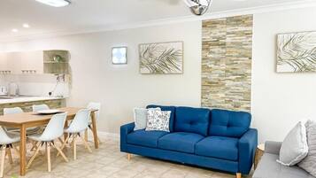 A modern living room with a blue sofa, dining table, and chairs.