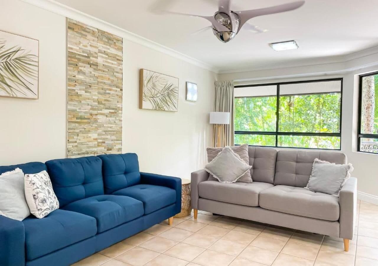 A living room with two sofas, a ceiling fan, and a large window with a view of greenery.