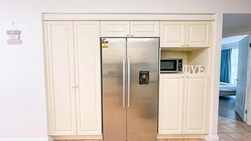 Un frigorifero in acciaio inox in una cucina con mobili bianchi e un forno a microonde sopra.