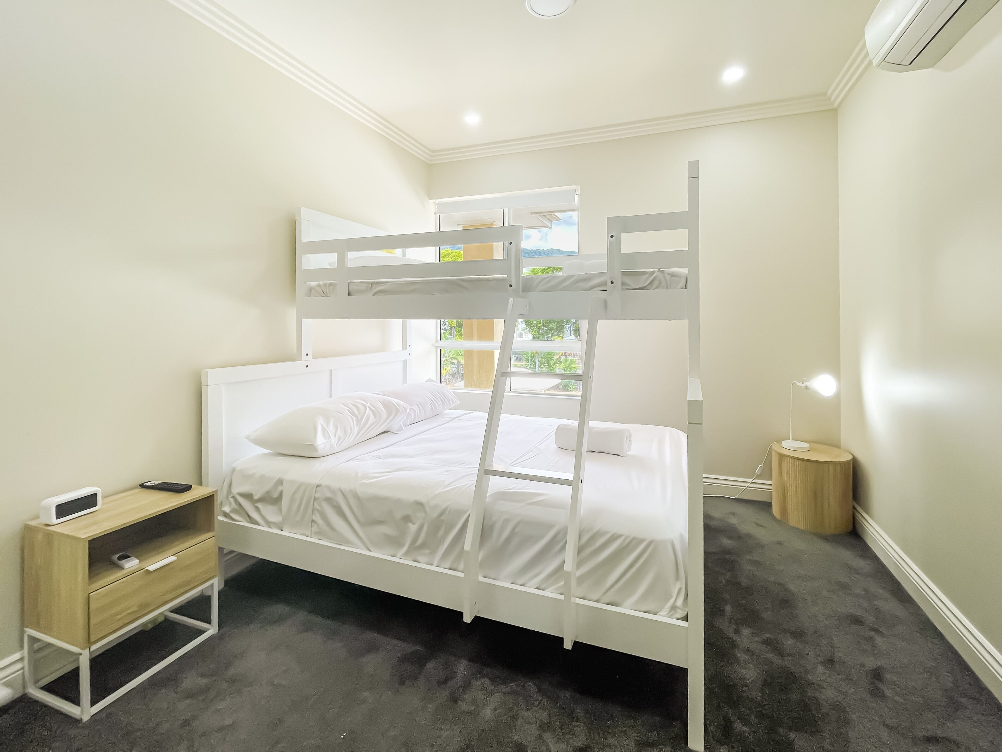 A bunk bed with white bedding, a bedside table with a lamp, and a small wooden cabinet.
