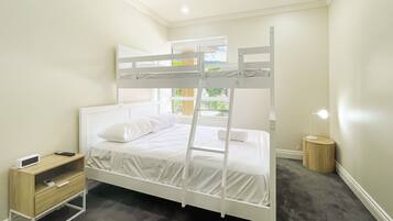 A bunk bed with white bedding, a bedside table with a lamp, and a small wooden cabinet.