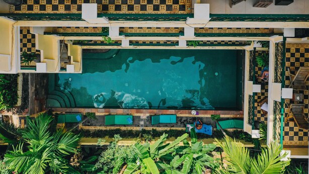 Oversigtsbillede af et hotel med en stor swimmingpool, udendørs siddepladser og et skakternet flisemønster på væggene.