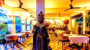 En restaurant med en Buddha-statue i midten, skakternet gulv og indendørs planter.