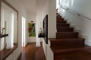 A modern staircase with wooden steps and a glass railing, leading to a landing with a colorful abstract painting and a mounted TV. - Relator Terrace. 3 bedrooms, 3 bathrooms, terrace & private pool (Sevilla)