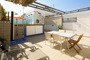 Un patio techado al aire libre con piscina, una mesa y sillas, y una escalera que lleva a un balcón.