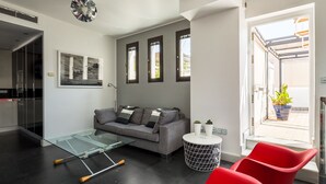 Un salon moderne avec un canapé gris, des fauteuils rouges, une table basse en verre et une petite table d’appoint agrémentée de plantes.