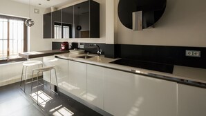 Une cuisine moderne dotée d’un grand îlot central, de meubles blancs et d’un plan de travail noir. On y trouve deux tabourets de bar, une machine à café et un évier.