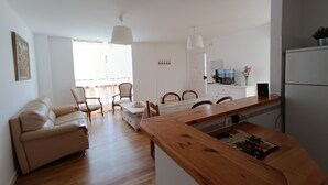 A modern living room with a sofa, dining table, chairs, and a kitchen area with a refrigerator and a TV. - Comfortable apartment renovated 2 steps from the beach (Málaga)
