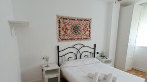 A bedroom with a bed, a ceiling fan, a bedside table, a nightstand, a wall tapestry, and a patterned rug. - Comfortable apartment renovated 2 steps from the beach (Málaga)