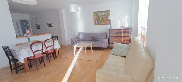 A living room with a sofa, a dining table with chairs, a coffee table, a dresser, and a painting on the wall.