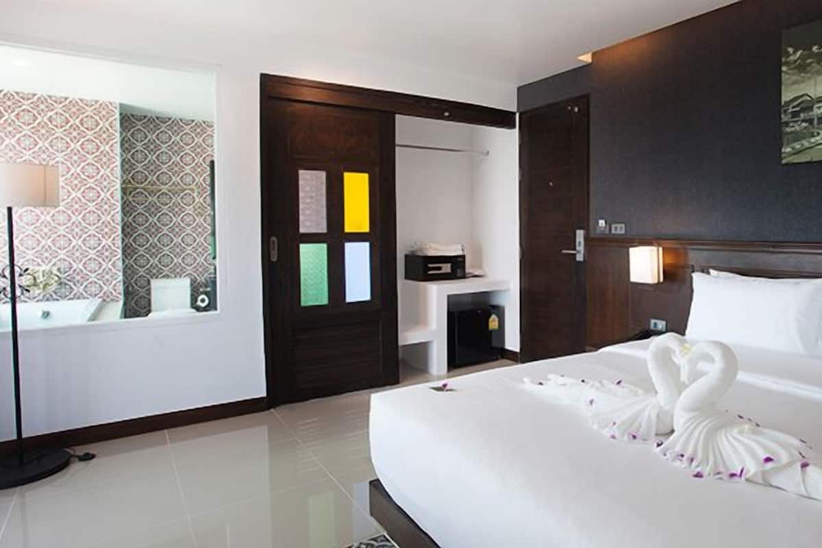 A hotel room with a large bed, a painting on the wall, and a door with colorful panels.