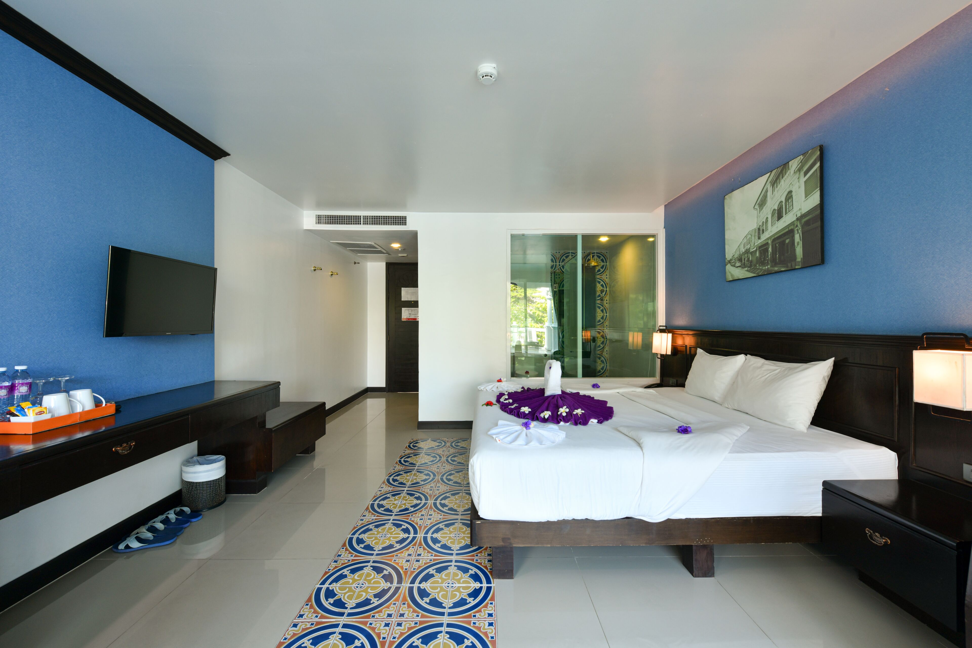 Una habitación de hotel con cama, televisión, escritorio y baño visible a través de una puerta de cristal.