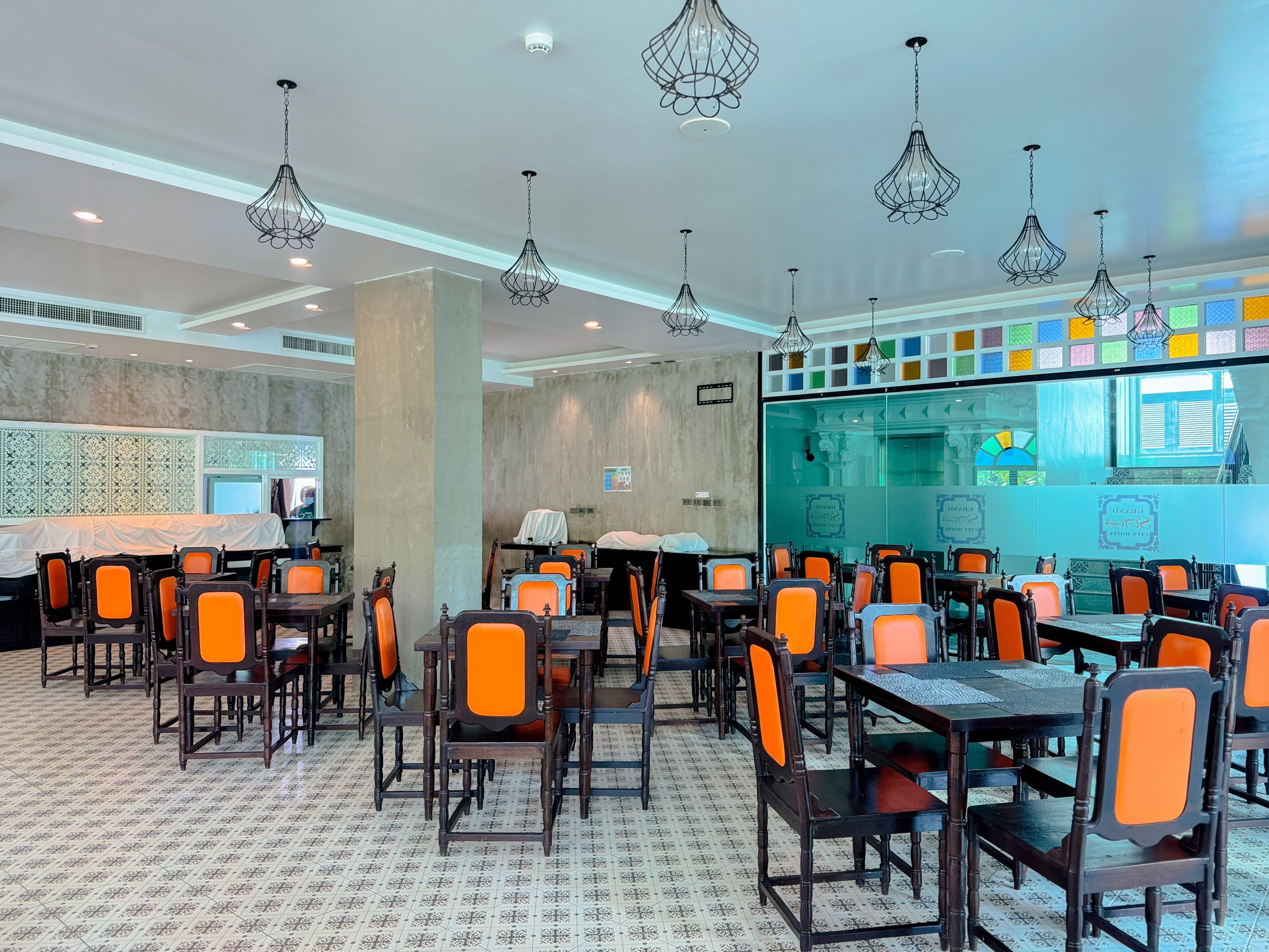 A restaurant with multiple tables and chairs, hanging pendant lights, and a patterned floor.