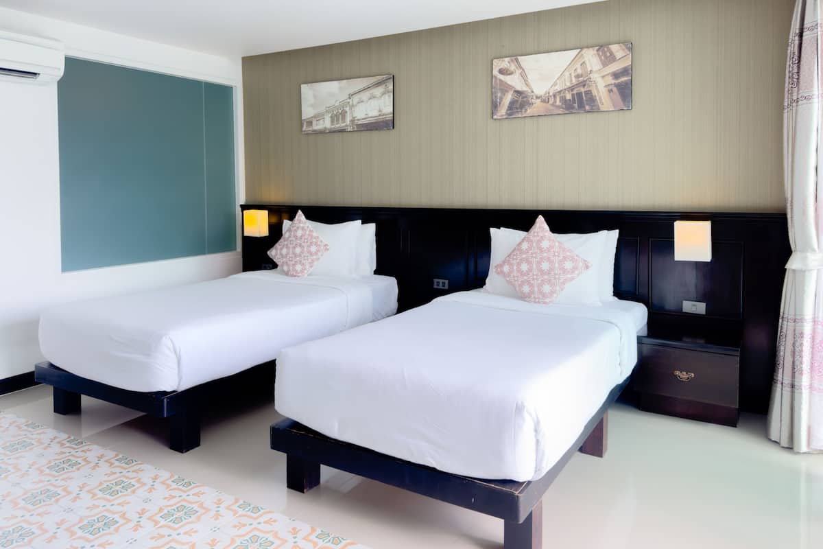 A hotel room with two single beds, a nightstand, a lamp, and two wall-mounted pictures.