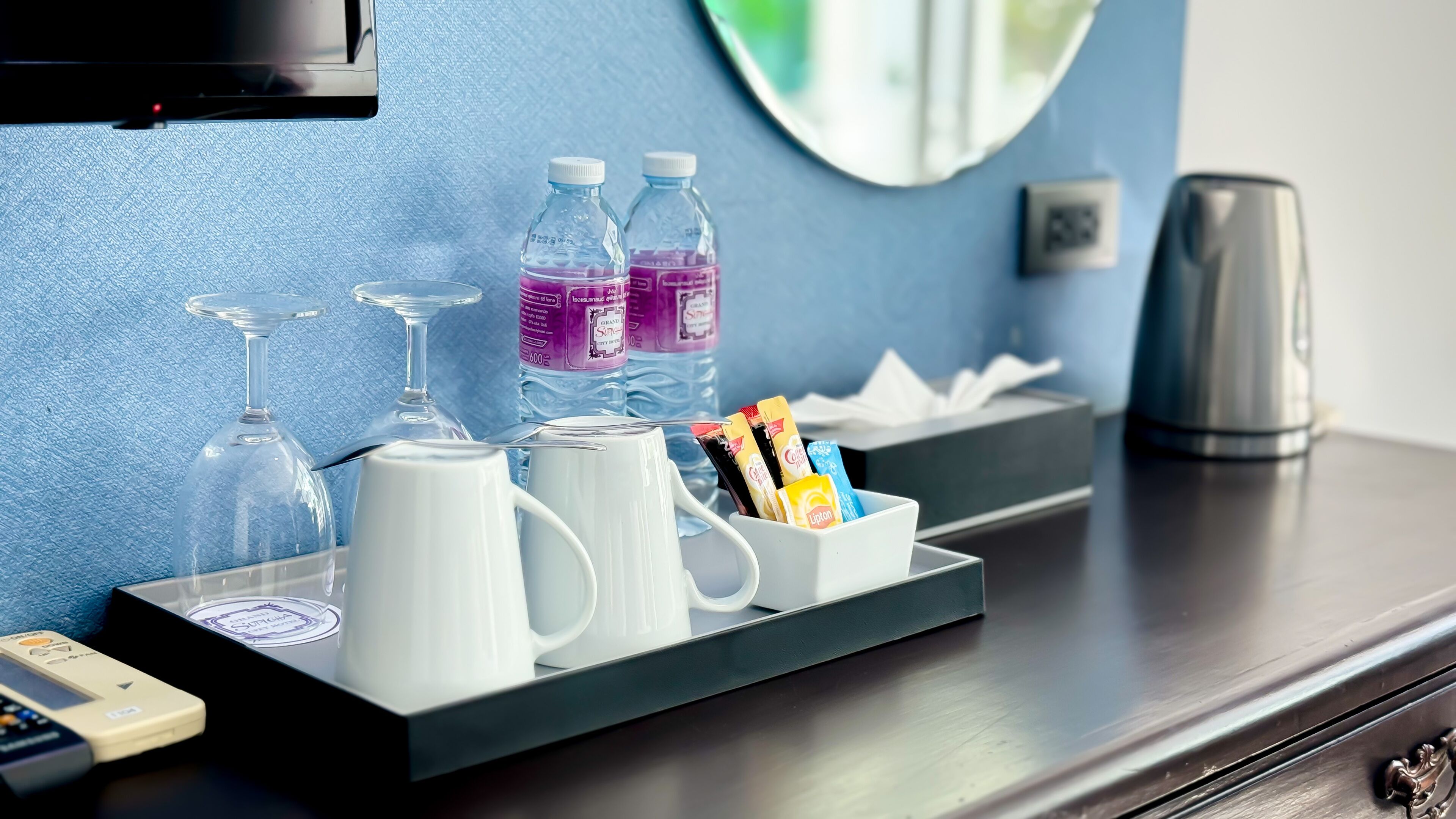 A hotel room's minibar with a tray containing a white mug, two bottles of water, a glass, and a box of snacks.