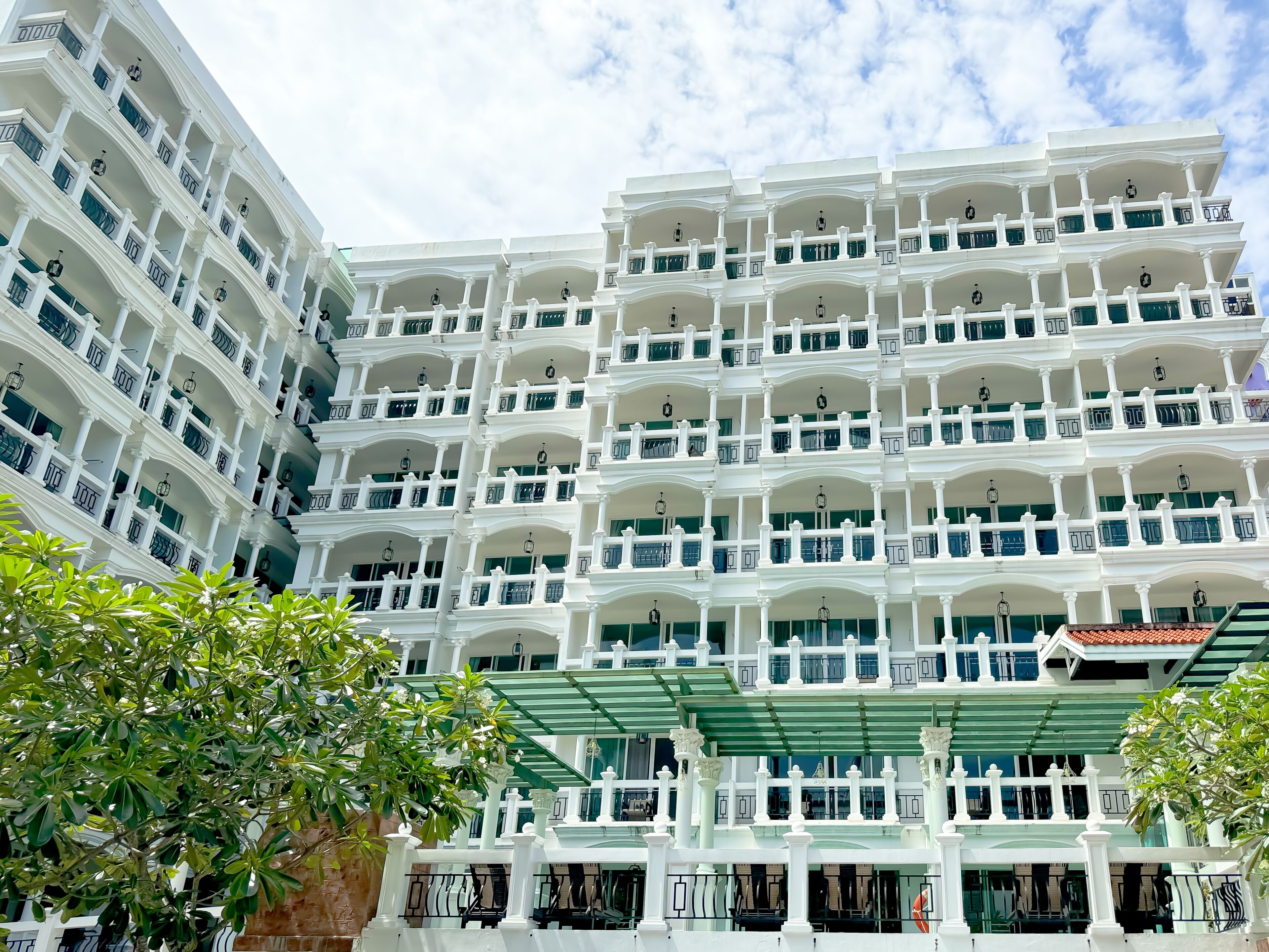 Un hotel de varios pisos con balcones, un toldo verde y un techo tradicional de tejas.