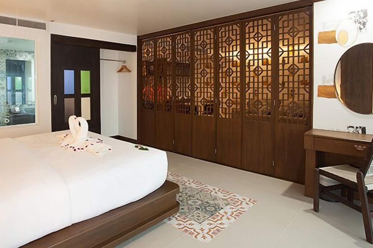 A bedroom with a bed, a wooden wardrobe, a desk with a chair, and a large mirror.