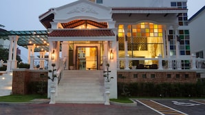 A hotel entrance with a covered porch, a staircase, and a large window with warm lighting. - Grand Supicha City Hotel (Phuket)