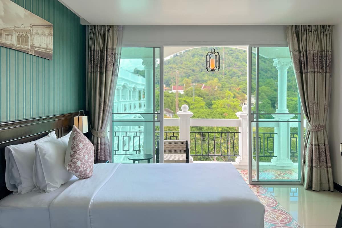 A hotel room with a large bed, a view of a balcony with a railing, and a hanging lantern.
