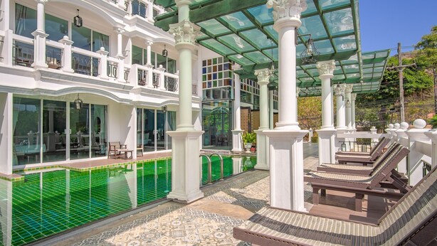 A covered outdoor area with a pool, lounge chairs, and a patterned floor. - Grand Supicha City Hotel (Phuket)