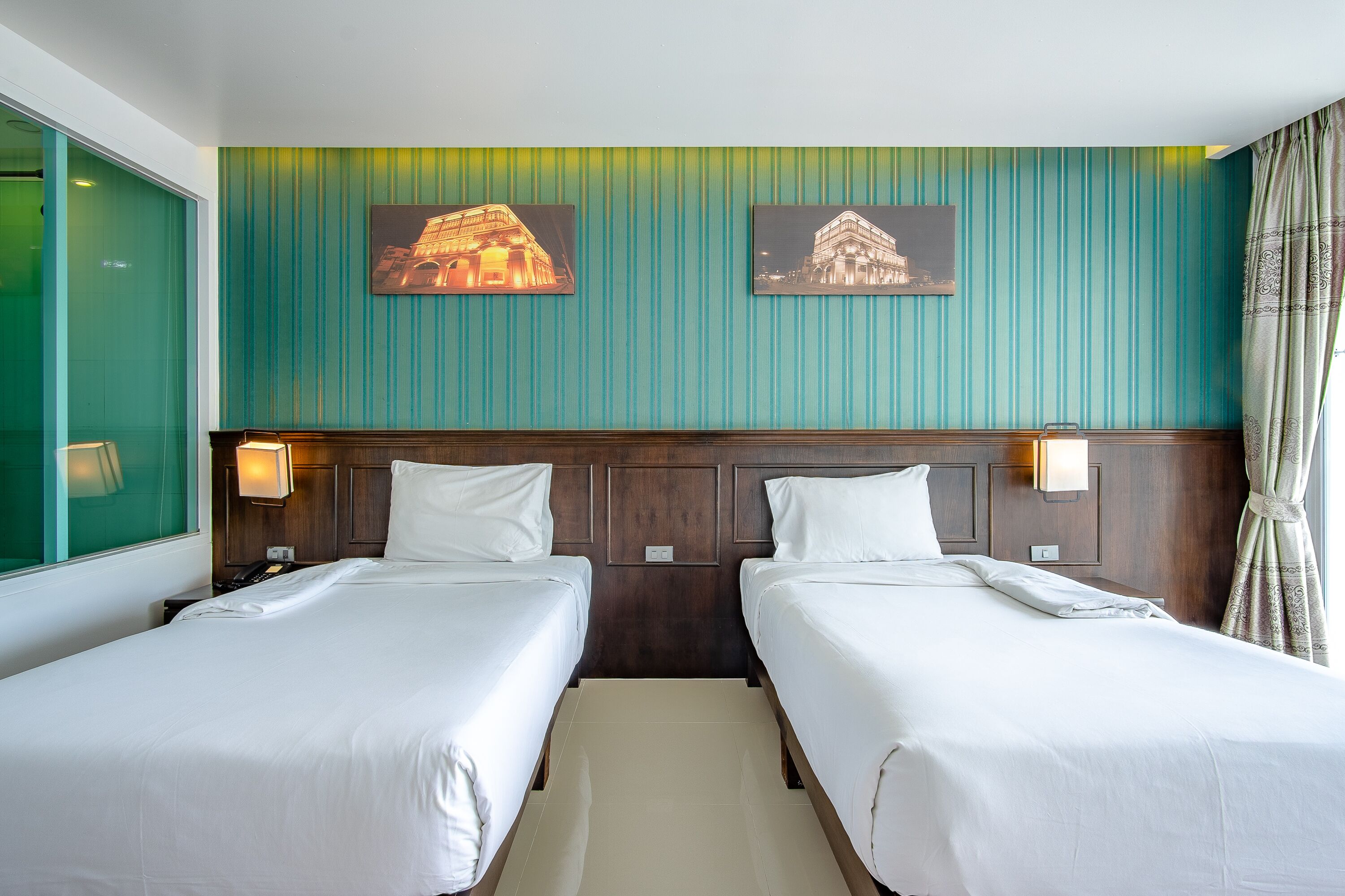 A hotel room with two beds, a wooden headboard, teal-striped wallpaper, and two framed pictures on the wall.