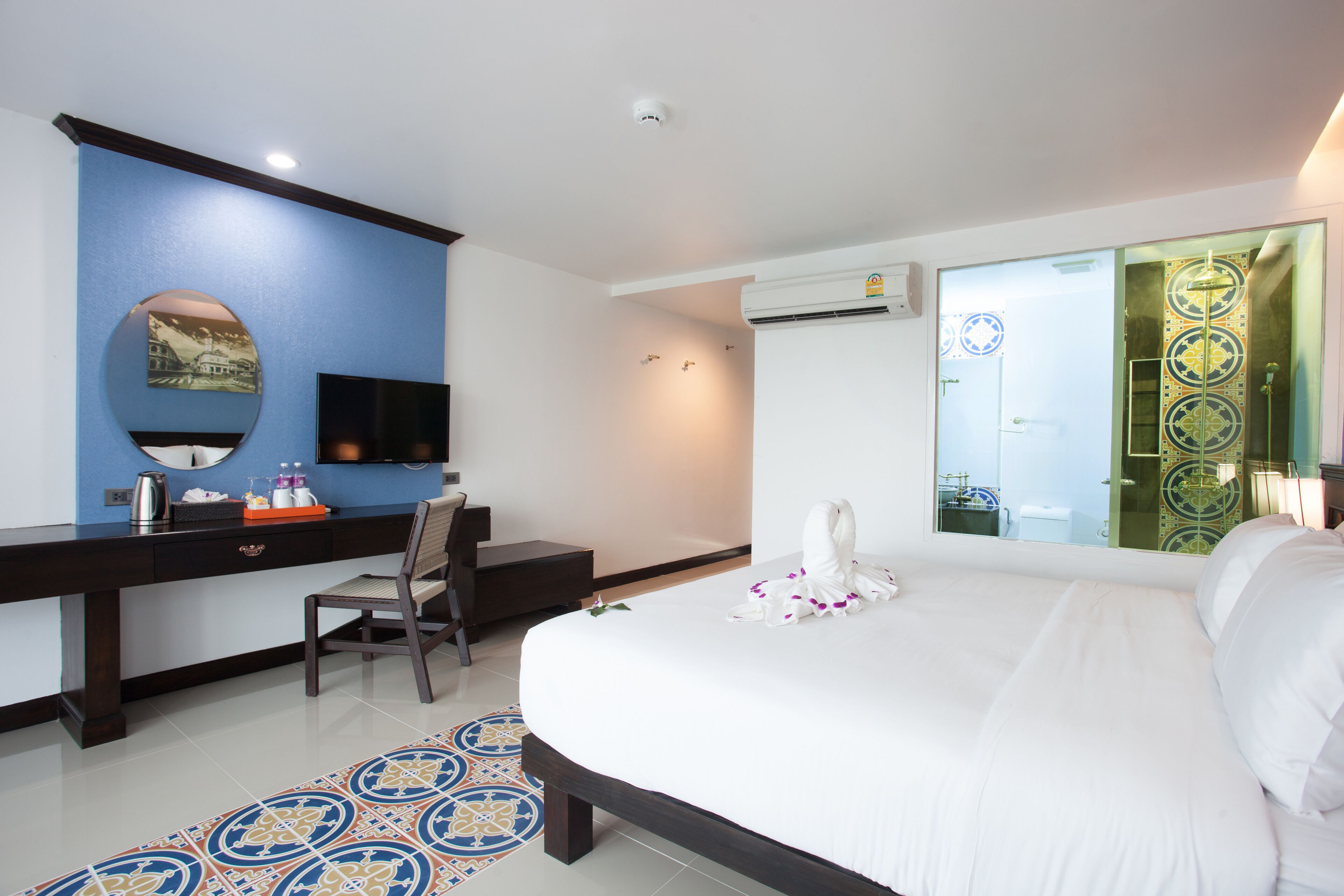 A hotel room with a large bed, a desk with a chair, a flat-screen TV, and a decorative mirror.