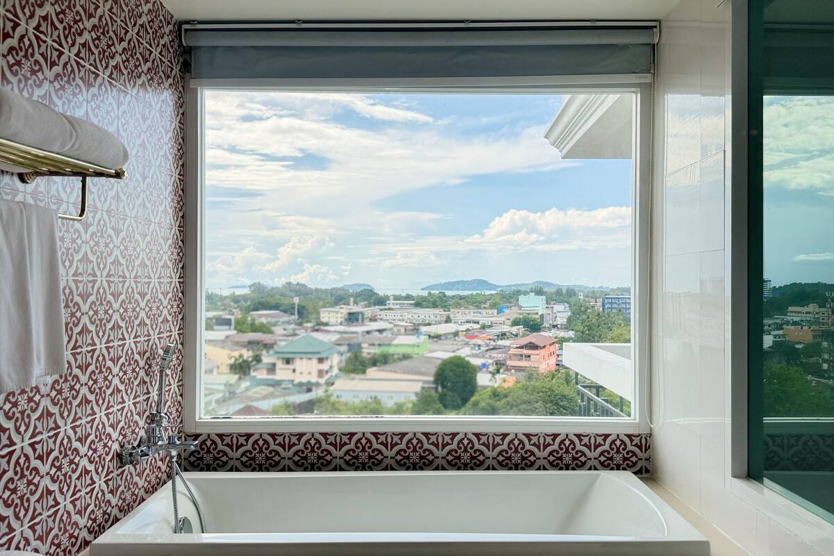A bathroom with a large window, patterned tiles, and a bathtub.