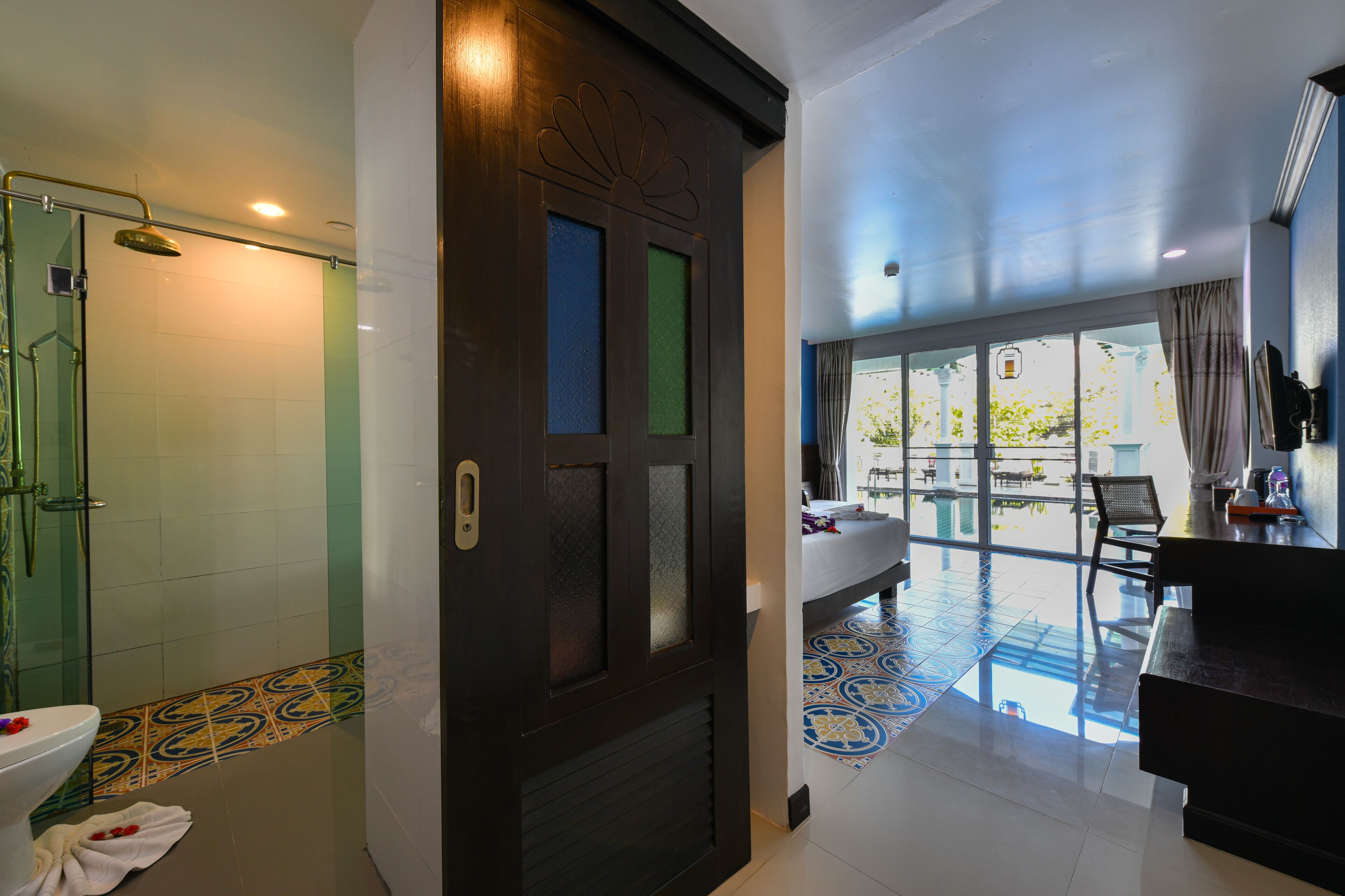 A hotel room with a shower, a bathroom with a toilet, a bed, a desk, and a view of the outside.