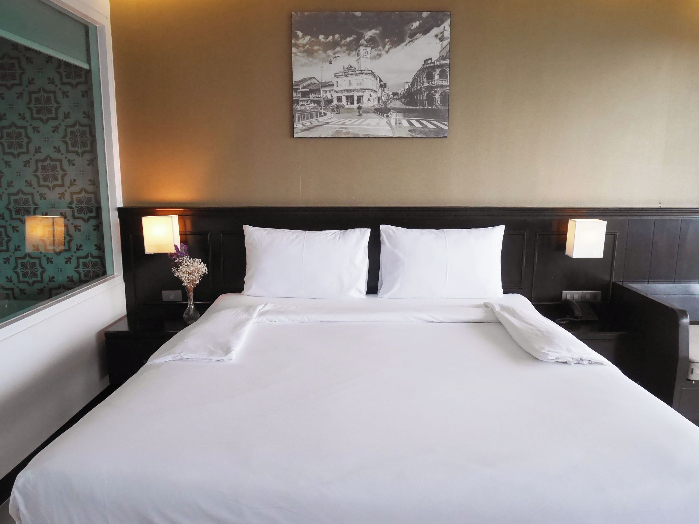 A hotel room with a large bed, two bedside lamps, a nightstand with a vase of flowers, and a wall-mounted picture.