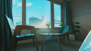Habitación de hotel con un ventanal grande, dos sillas de madera, una mesita y una planta en maceta.