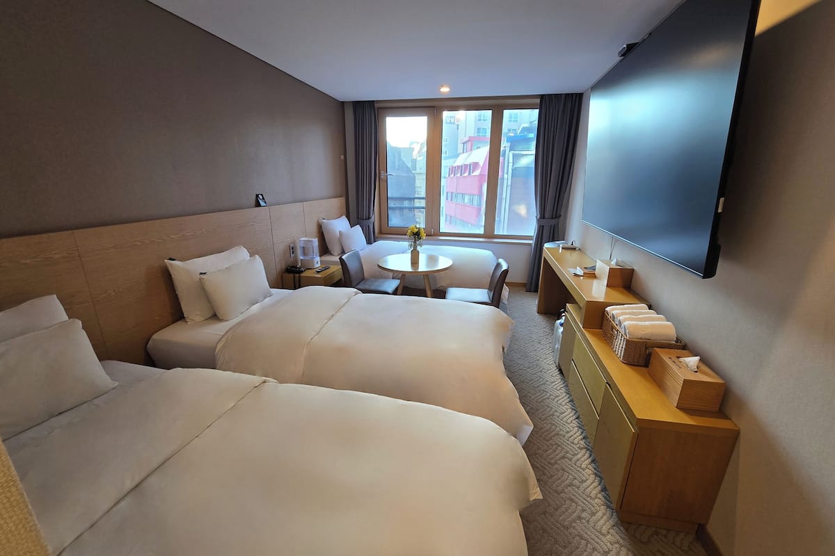 Een hotelkamer met twee bedden, een bureau, een stoel, een tafeltje, een televisie en een raam met gordijnen.