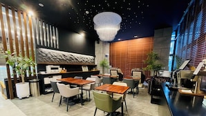Interior de un restaurante moderno con mesas y sillas de madera, una zona de bar y plantas decorativas.