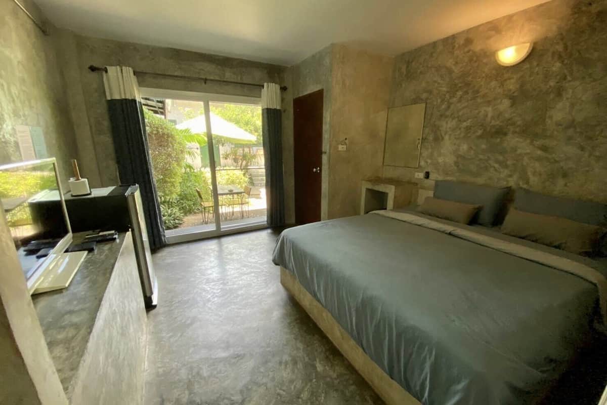 A bedroom with a large bed, a desk, and a sliding glass door leading to an outdoor area.
