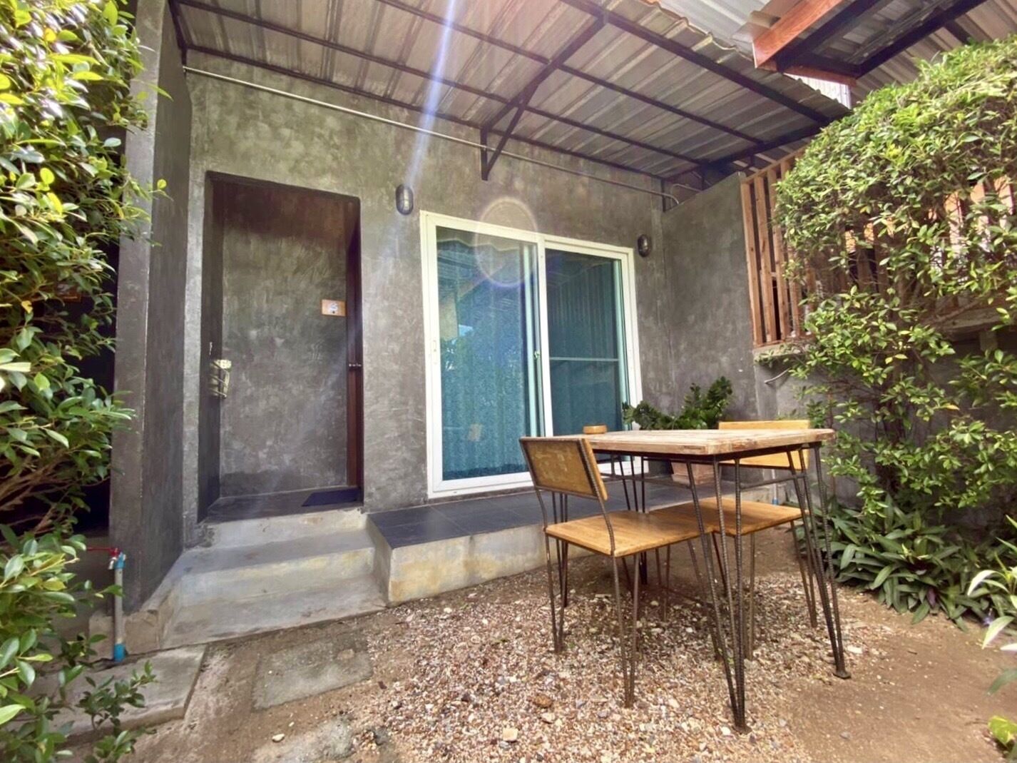 A patio area with a concrete floor, a wooden table with metal chairs, a sliding glass door, and a metal roof.
