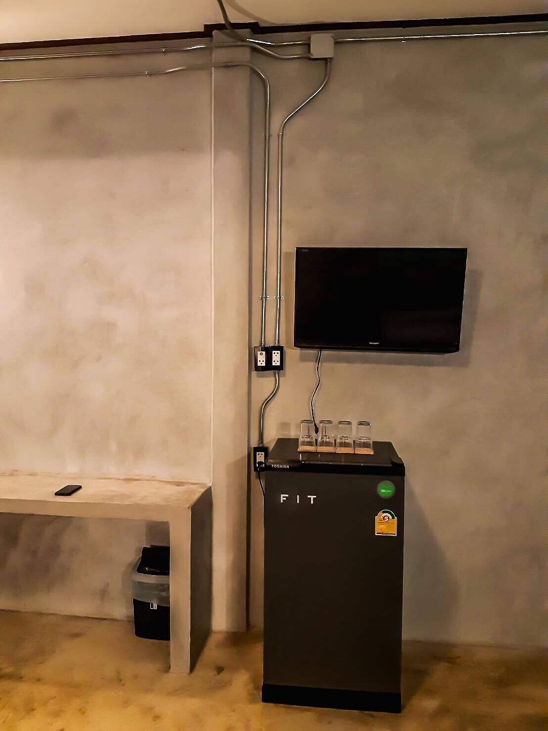 Una habitación con un banco, un mueble negro con luz verde y un televisor montado.