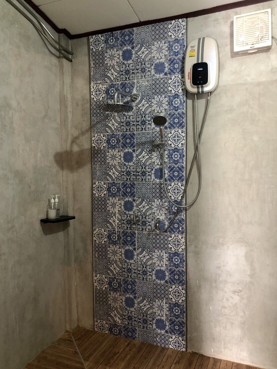 Eine Dusche mit blau-weißen Fliesen, einer Handbrause, einer fest montierten Bedienfeld und einem kleinen Ablagebereich für Toilettenartikel.