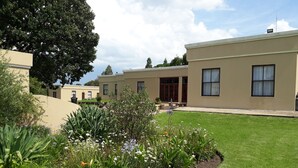 A modern building with a flat roof, large windows, and a well-maintained lawn with various plants and flowers. - The Guest House (Lekwa)