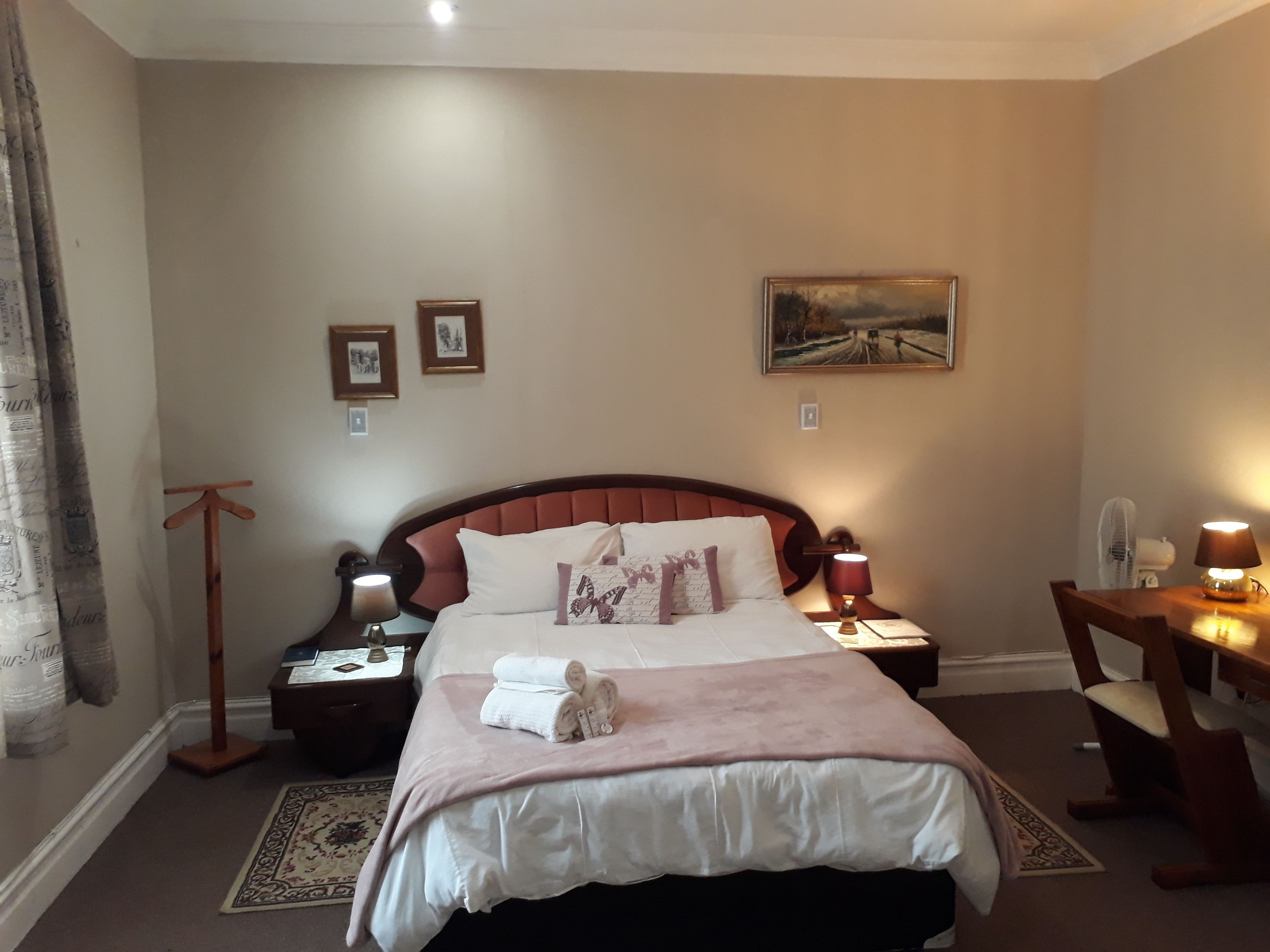 A neatly arranged bedroom with a large bed, bedside lamps, a desk, and a chair.