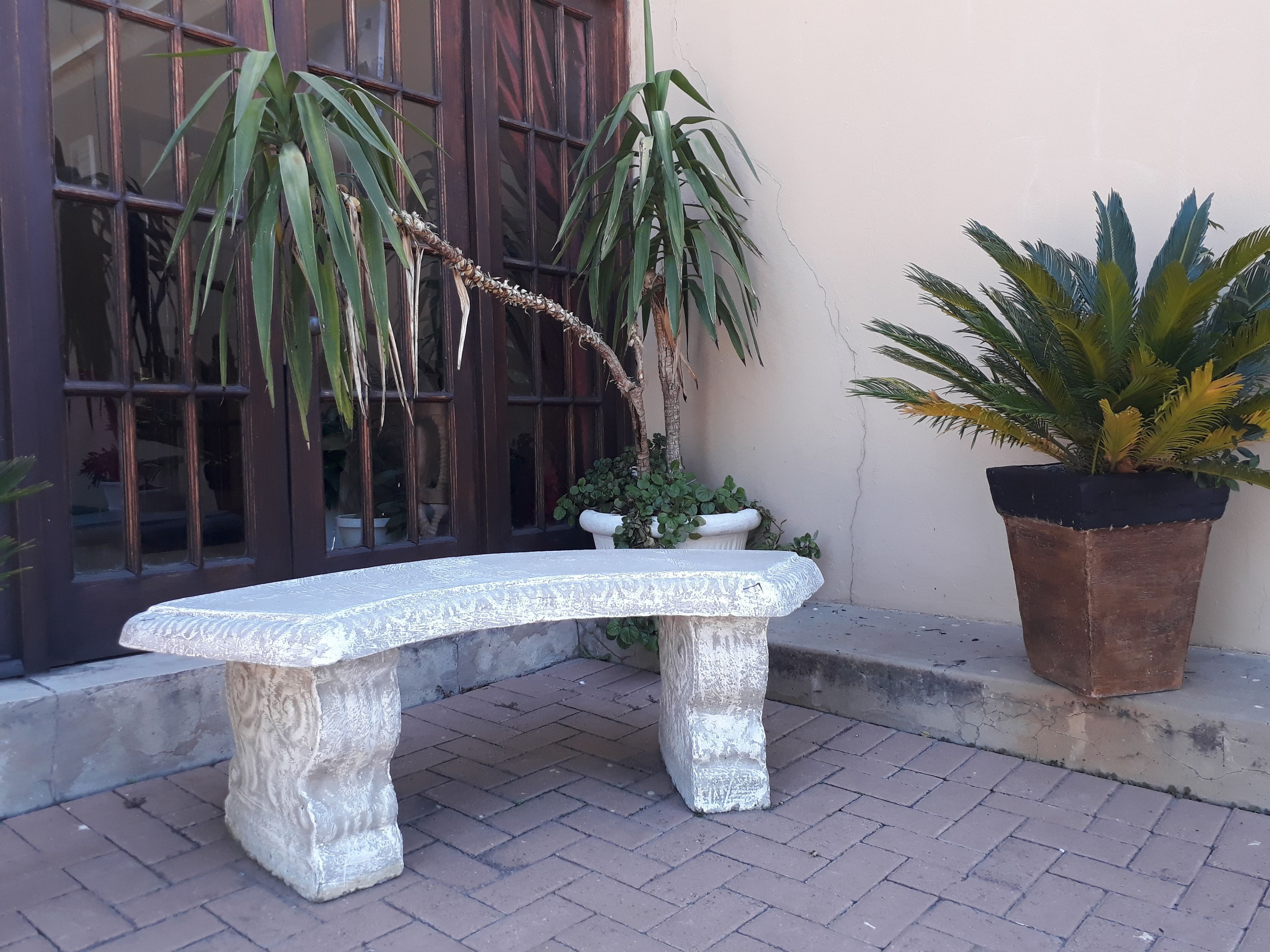 A stone bench with a textured surface, positioned on a brick-paved area.