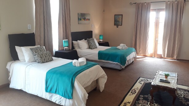 A hotel room with two beds, a small table with a remote control, and a decorative rug. - The Guest House (Lekwa)