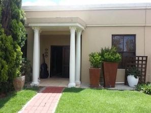 A building with a covered entrance, columns, and potted plants.