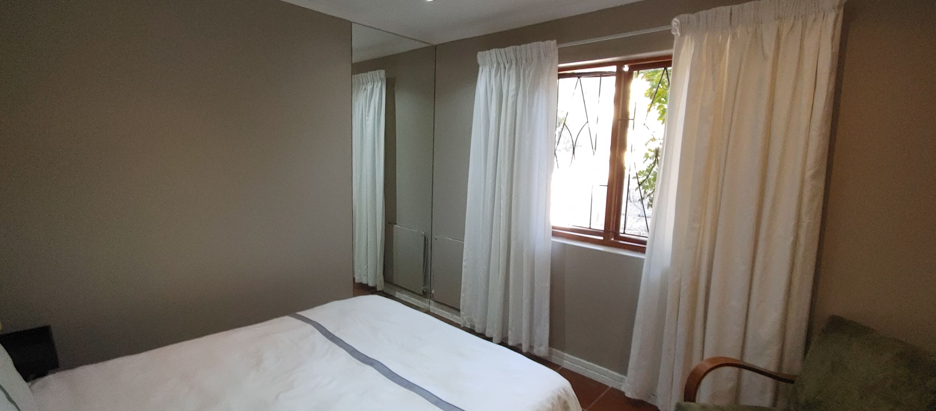 Un dormitorio con cama, una silla y una ventana con cortinas.