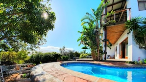 A swimming pool with a curved edge, surrounded by stone steps and lush greenery. - Happy Home Imhoffs Gift (Cape Town)