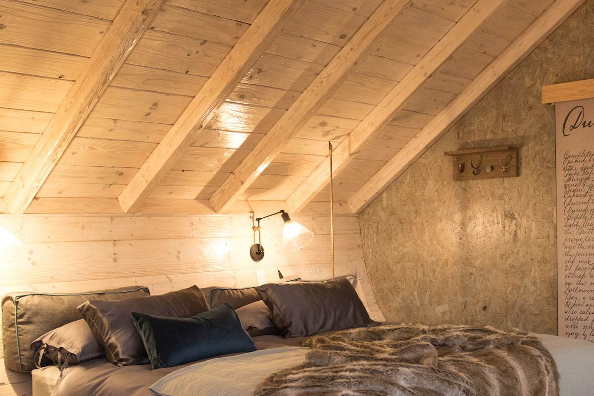 A cozy bedroom with a wooden ceiling, a bed with multiple pillows, and a rug on the floor.