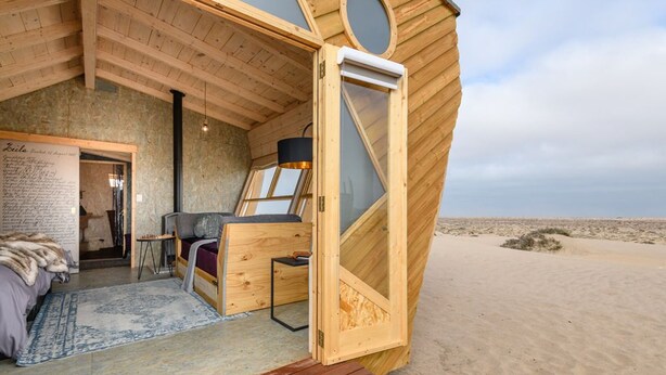 Una stanza circolare in legno con un letto, una scrivania, una finestra e vista sulla spiaggia.