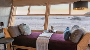 Una camera accogliente con un letto di legno, un tavolino con un bollitore e vista sulla spiaggia attraverso ampie finestre.